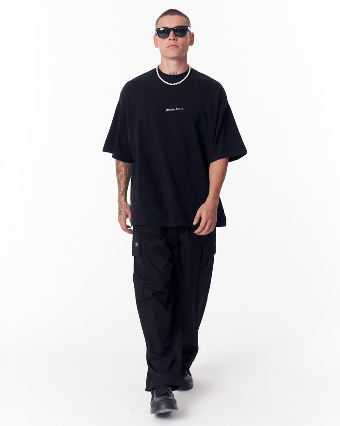 Martin Valen black oversized T‑shirt front view, mid‑body shot with model wearing sunglasses and pearl necklace