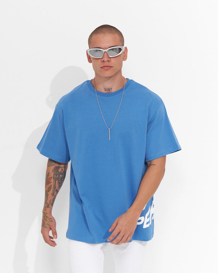Martin Valen ’Perspective’ oversized blue T‑shirt front close‑up with white sunglasses and silver chain necklace