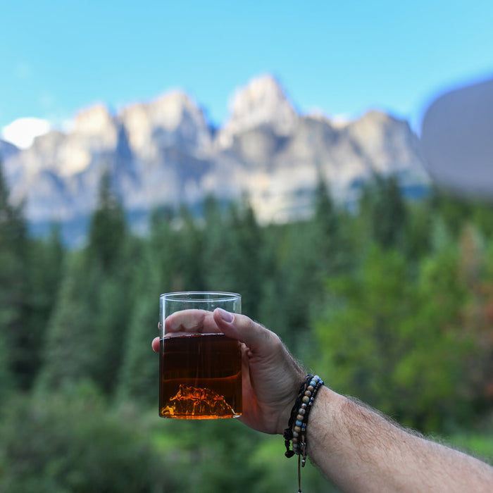 Hand holding MTNPK Castle Mountain glassware with forest and mountain view, sold at Greenbriar Market Calgary