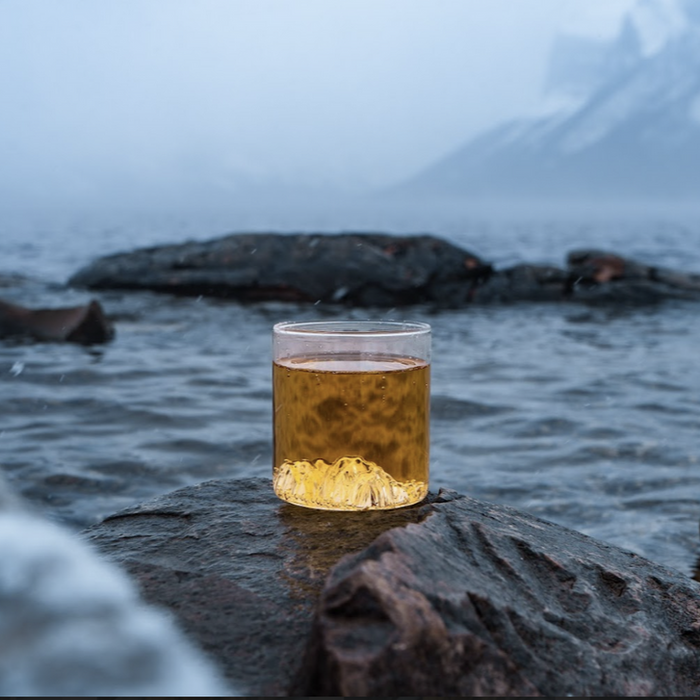 MTNPK Lake Minnewanka tumbler glass on wet rock with lake backdrop, available at Greenbriar Market Calgary