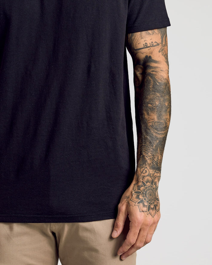 Person wearing Black Classic Polo and light tan pants, showcasing tattooed forearm.