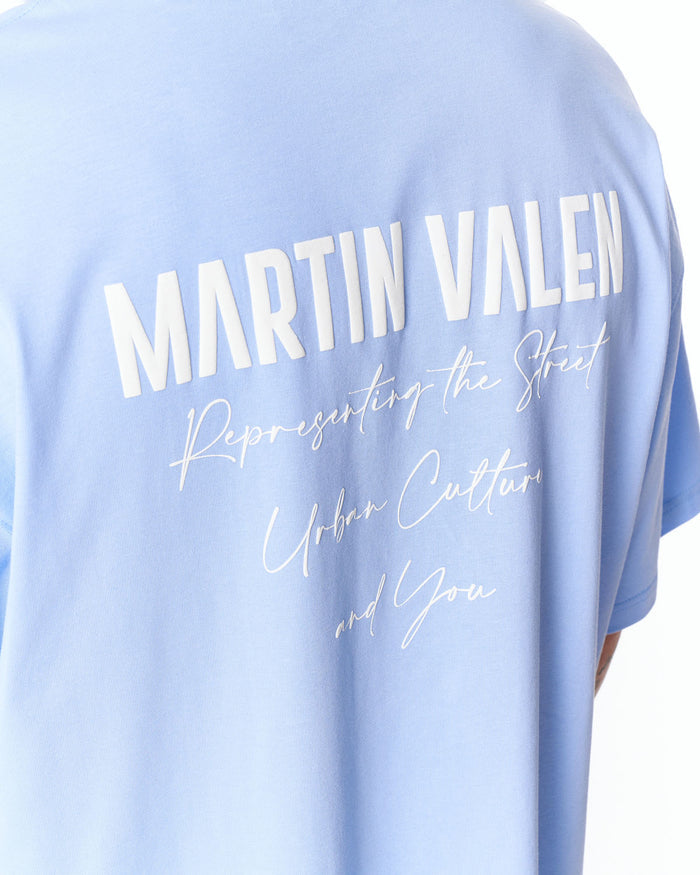 Martin Valen blue "Slogan" oversized T‑shirt close-up of back showing large white Martin Valen uppercase print and script details below